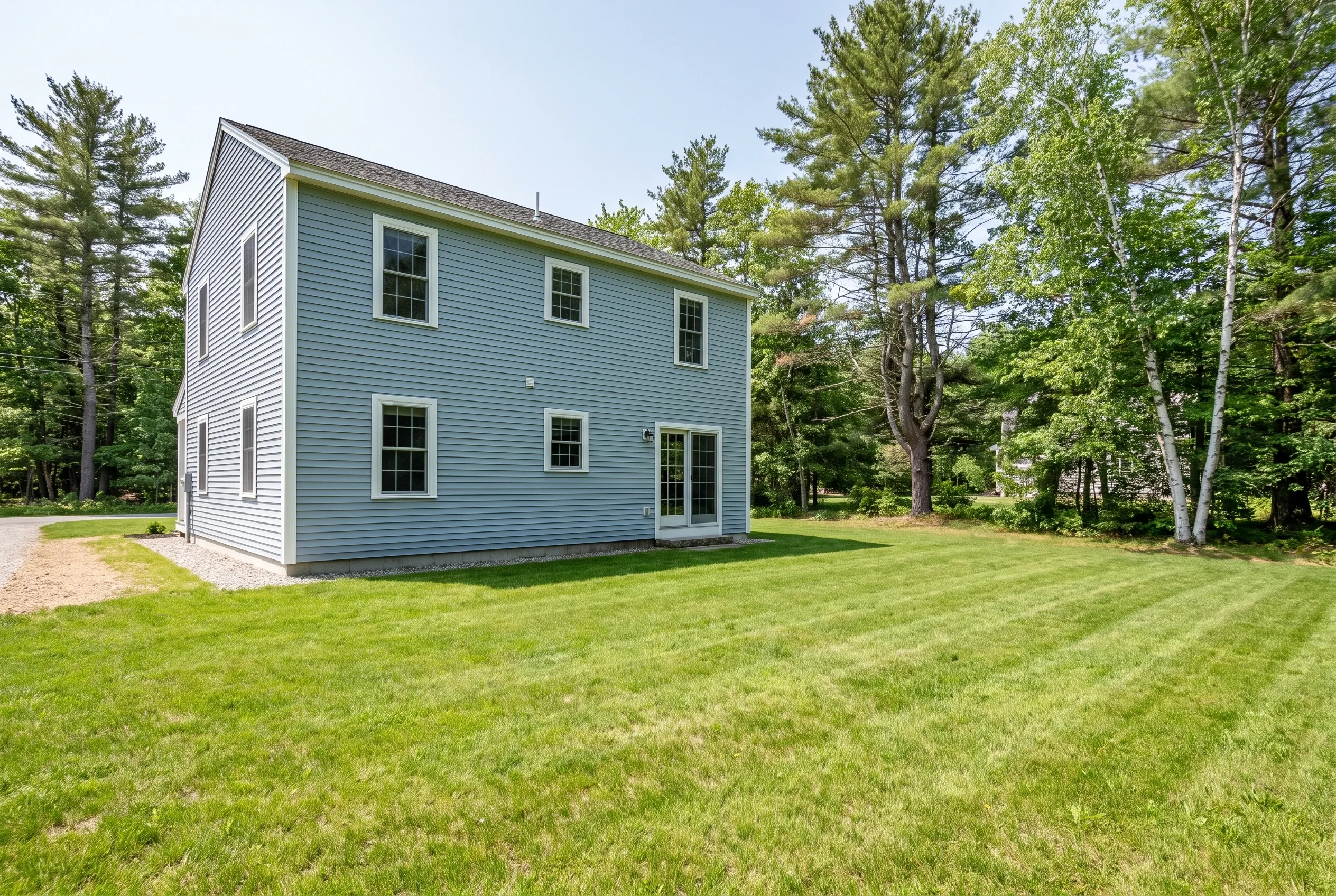 Open mowed backyard lawn behind a blue-gray two-story house with no deck, bordered by pine and birch trees