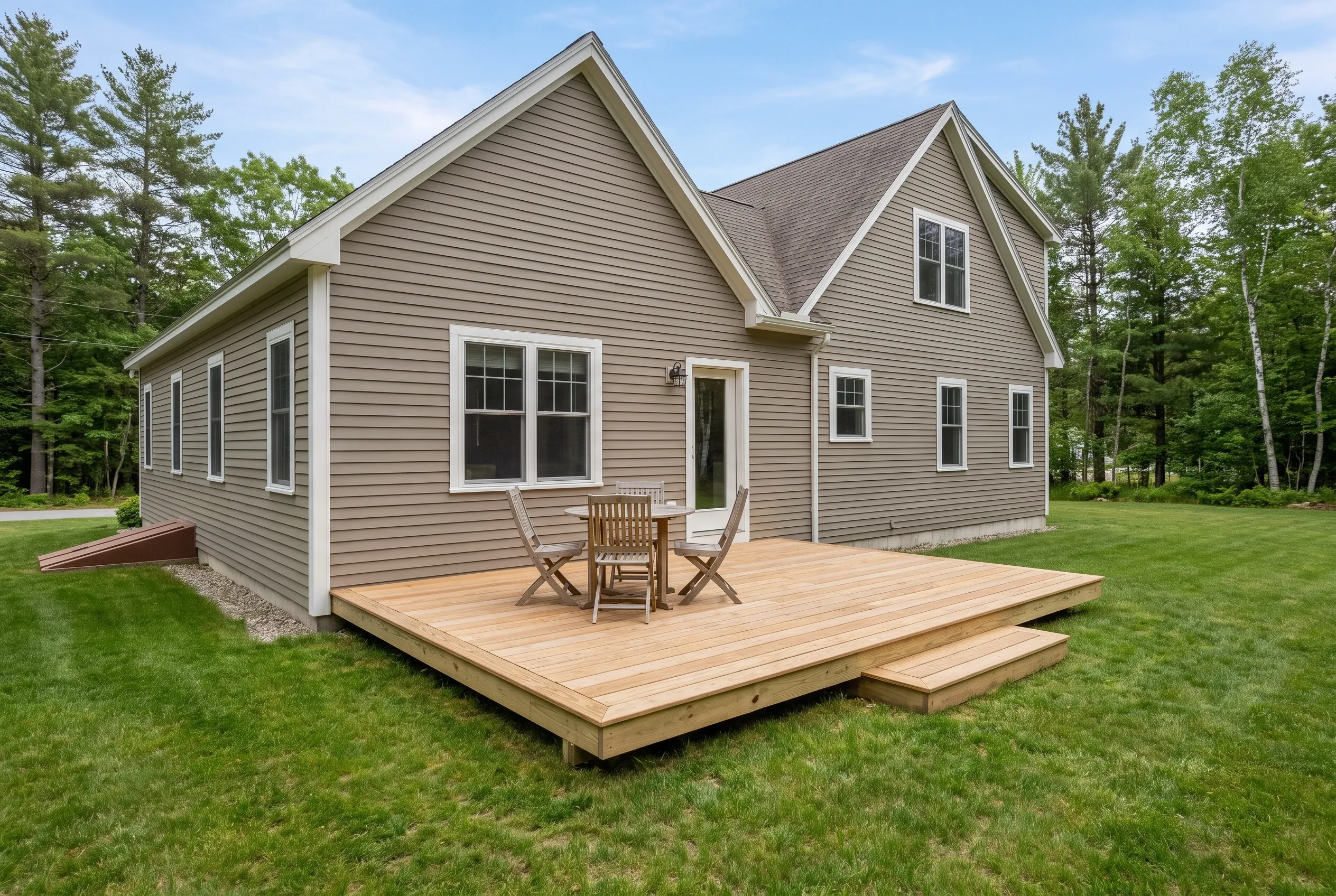 Low wood deck with a single step, wooden table and chairs, attached to the back of a tan two-story house