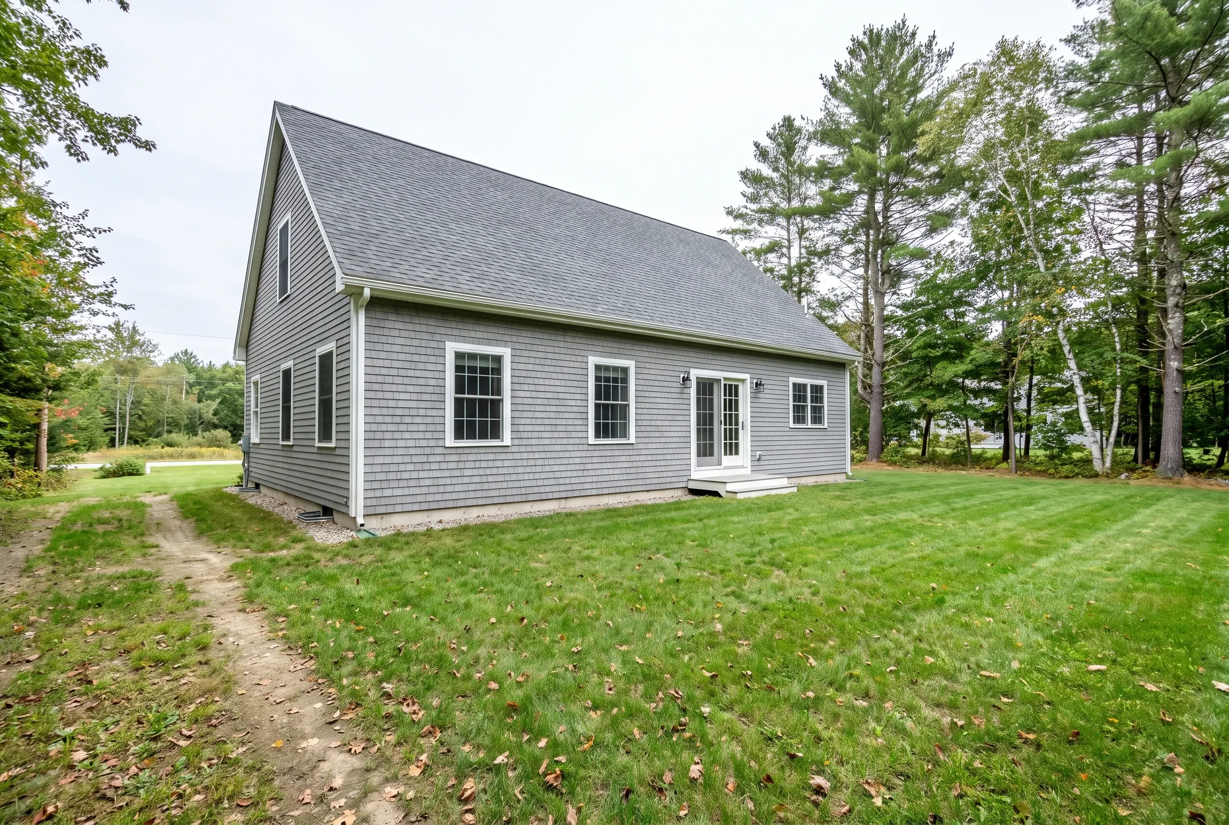 Gray shingled house with a rear door and small stoop on a wide lawn crossed by a worn dirt footpath