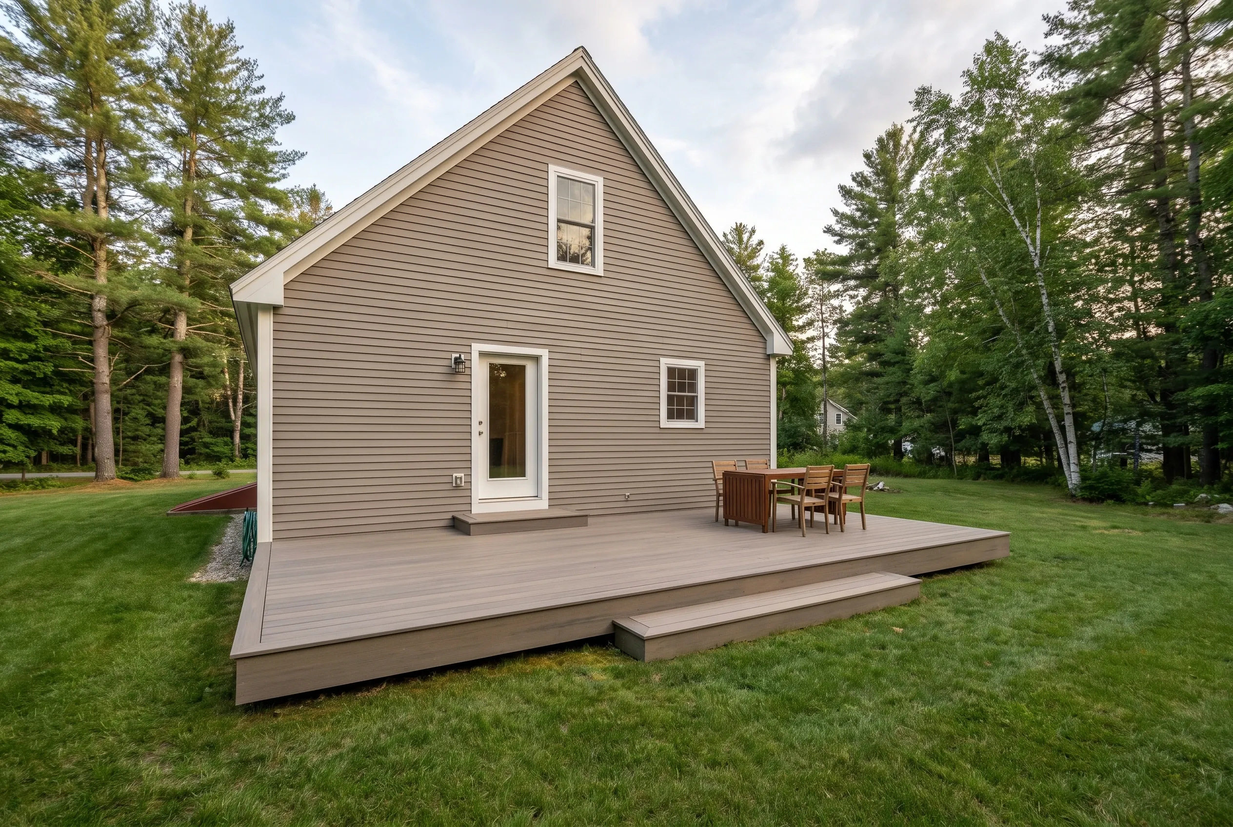 Deck builders in Raymond, ME: low gray-brown deck with a broad step, table and chairs beside a tan sided house